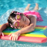 "Girl with styrofoam swimming board" by Tommy Wong via Wikimedia Commons (2006 - CreativeCommons) -- English: A young girl taking a break in a swimming pool, grabbing on to a rainbow-coloured styrofoam flotation device.